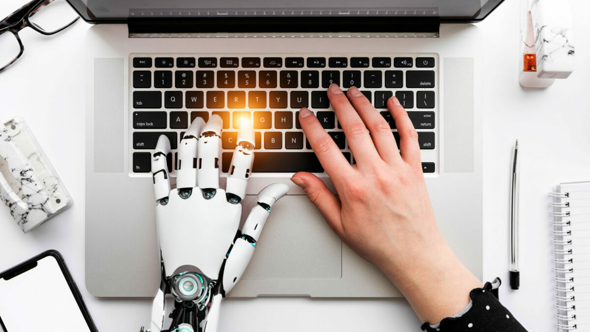 Eine Roboter Hand und eine normale Menschenhand tippen gleichzeitig auf einer Macbook Tastatur