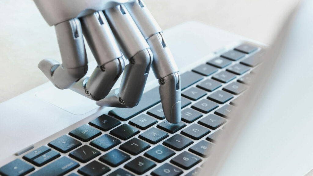 Roboter Hand tippt auf einen Buchstaben auf einer Macbook Tastatur